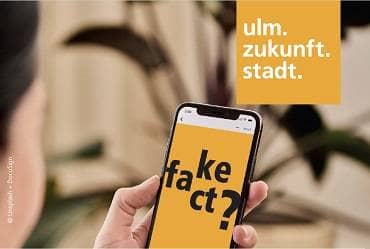 Eine Person die ein Smartphone bedient, auf dem der Schriftzug "Fake Fact?" in schwarzer Schrift auf gelbem Grund abgebldet ist © Unsplash + DocuSign