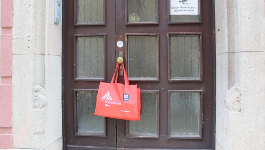 Eine rote gefüllte Tasche, die an einemTürknauf einer braunen Türe hängt