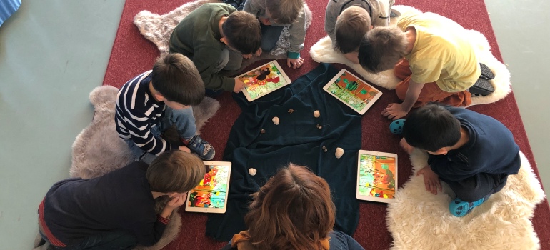 Ein Kreis von Kindern, die eine Vorlese-App auf Tablets nutzen, von oben fotografiert