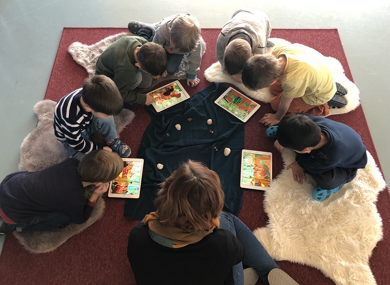 Ein Kreis von Kindern, die eine Vorlese-App auf Tablets nutzen, von oben fotografiert