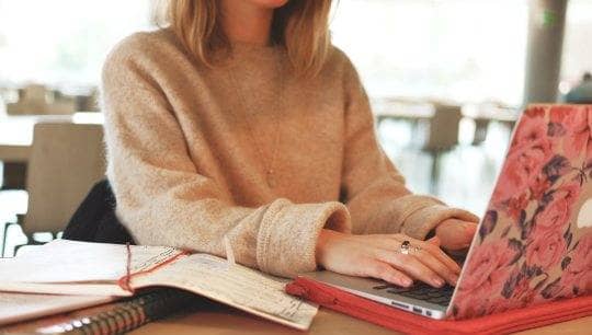 Eine blonde Frau sitzt an einem aufgeklappten Laptop mit Blumenmuster auf dem Laptopdeckel