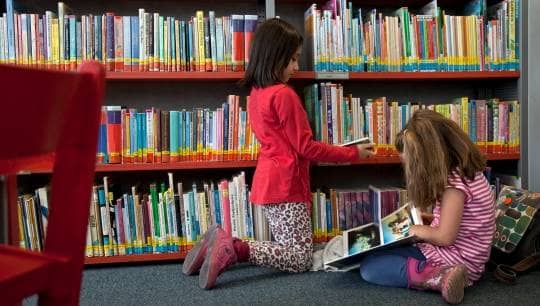 Zwei Kinder beim Lesen an einem Bücherregal